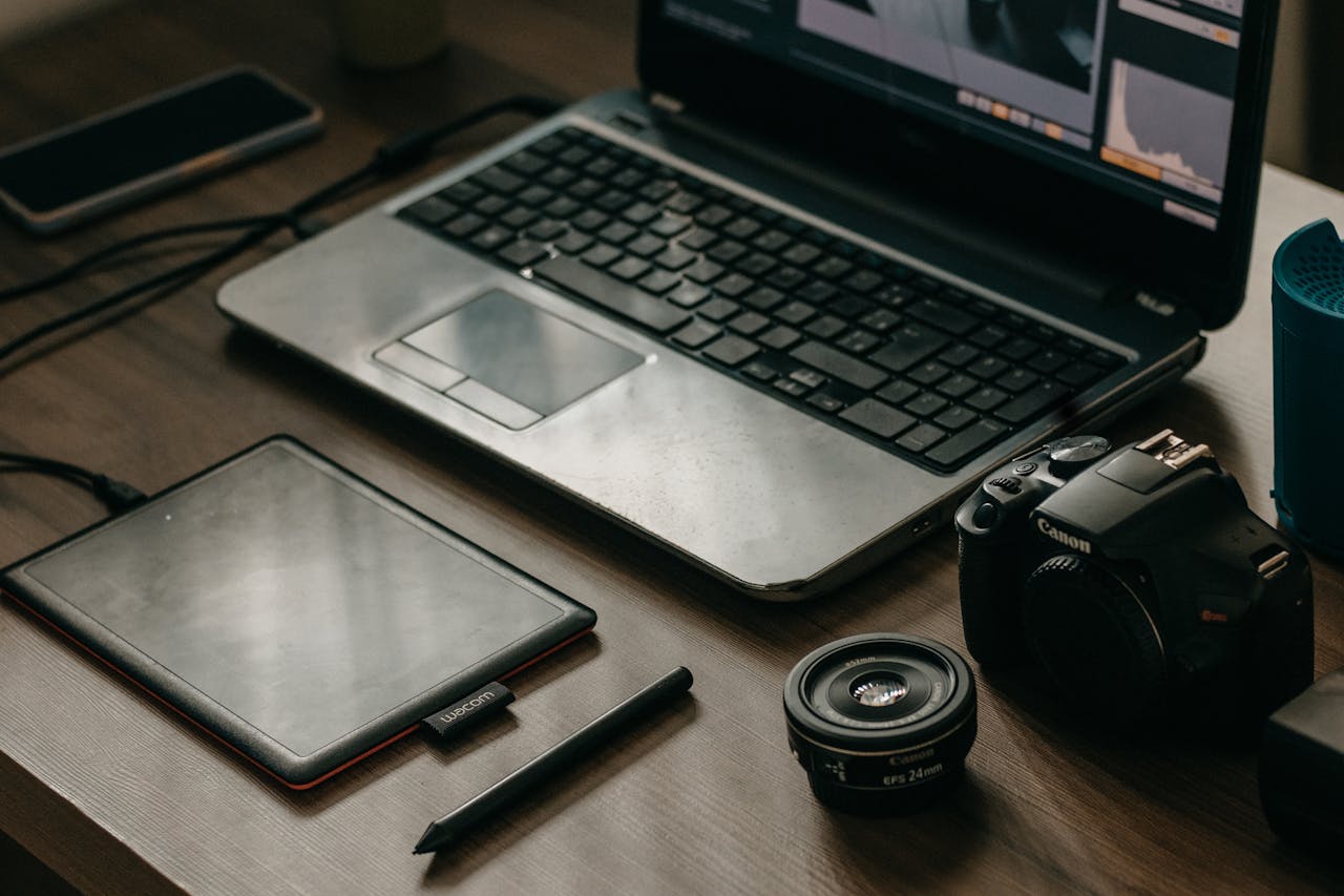 Laptop, camera, lens, and graphic tablet on a desk for digital creatives.